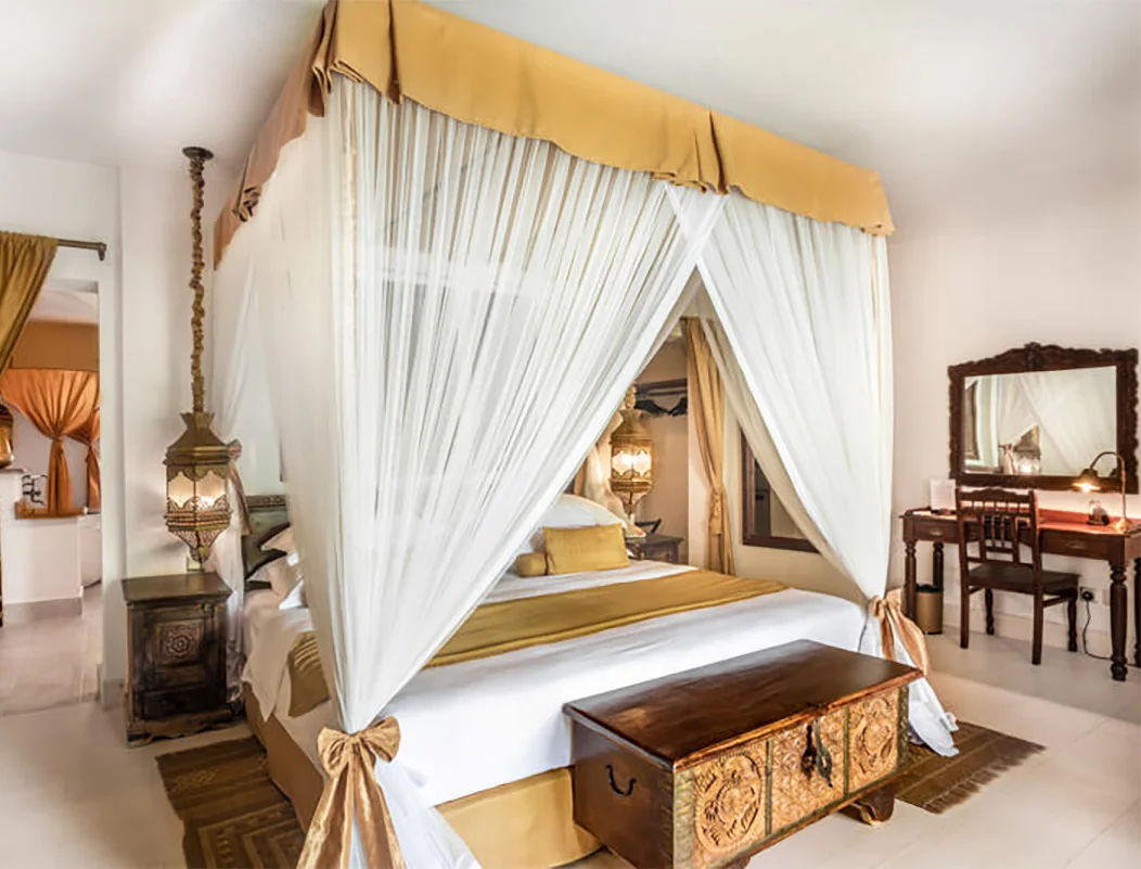 Canopy bed with white drapes and a carved wooden chest at Baraza Resort & Spa