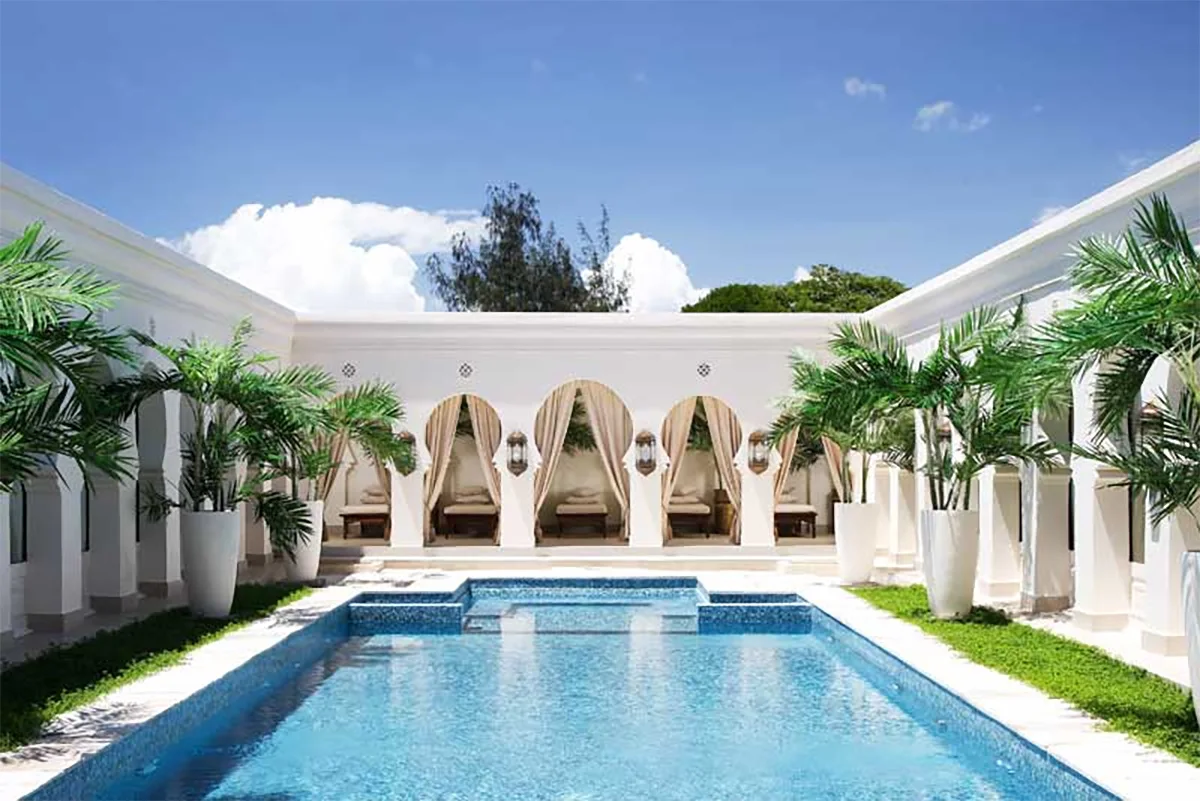 Swimming pool in a white courtyard lined with arches and palms at Baraza Resort & Spa