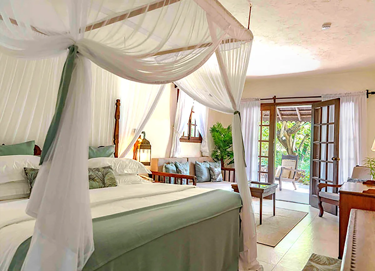 Canopy bed with white drapes and doors open to a garden at Breezes Beach Club & Spa