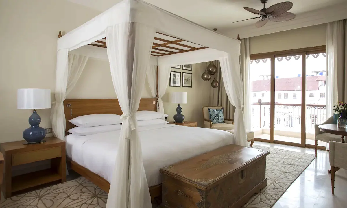 Canopy bed and wooden chest in a bright room with a balcony at Park Hyatt Stone Town