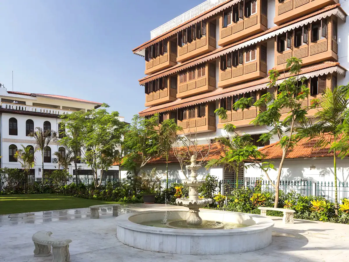 Park Hyatt Stone Town building with wooden balconies beside a garden fountain