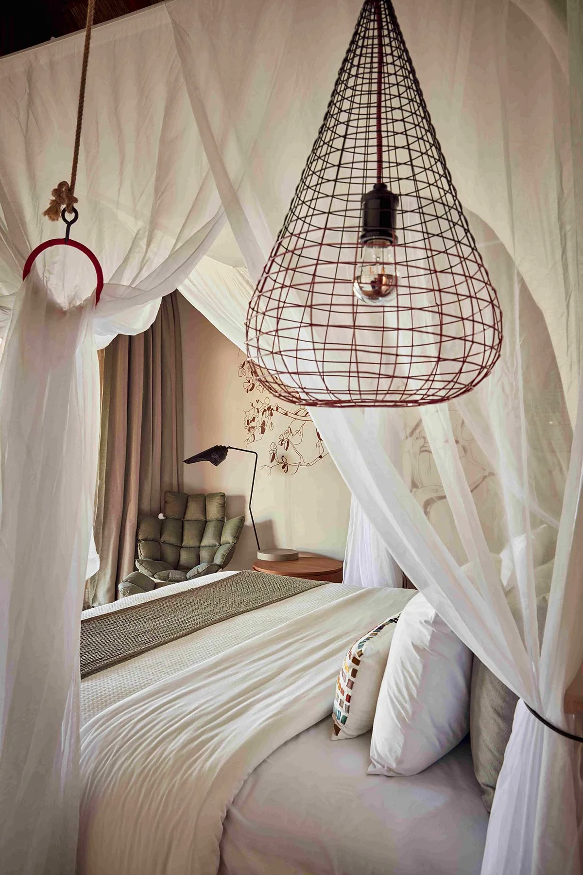 Bed with white canopy and a wire pendant lamp in a bungalow at Zuri Zanzibar