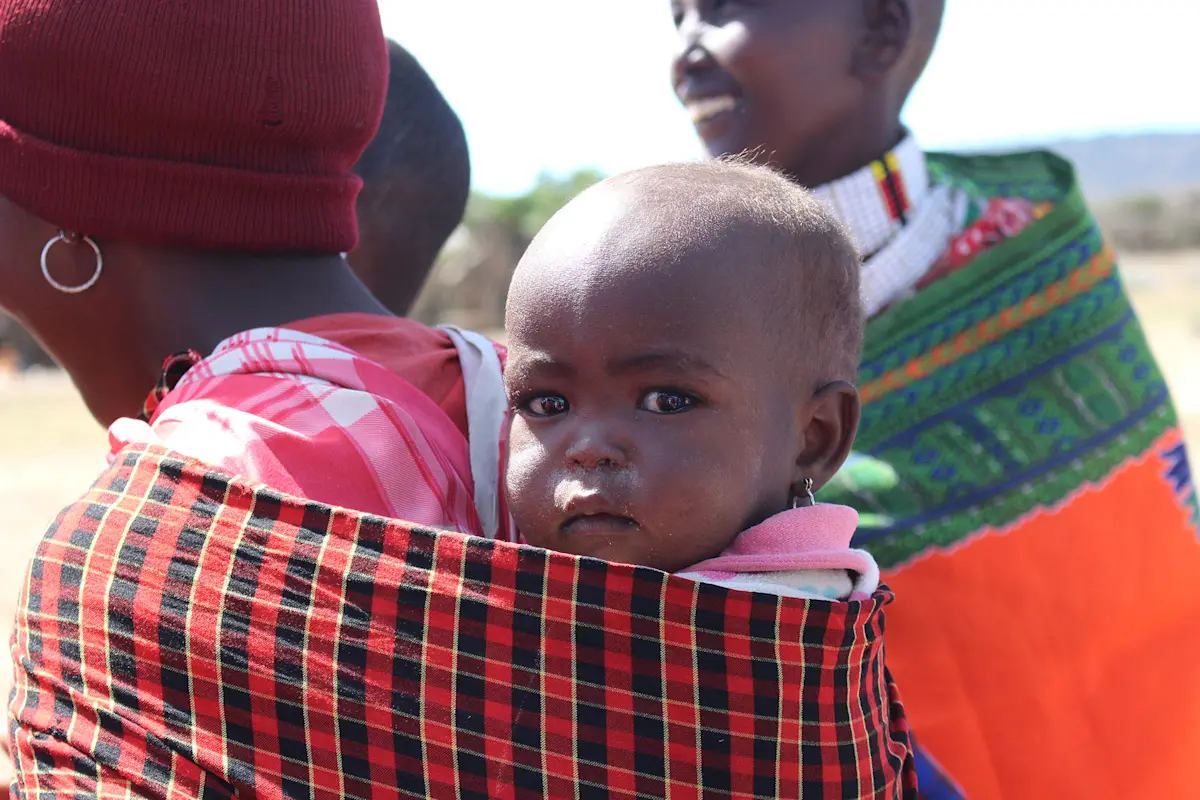 Maasai baby carried on a woman's back in a red checked shuka