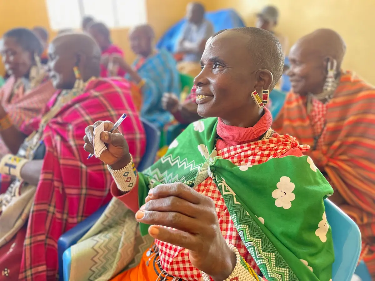 Maasai woman in a green kanga holding a pen at a community workshop