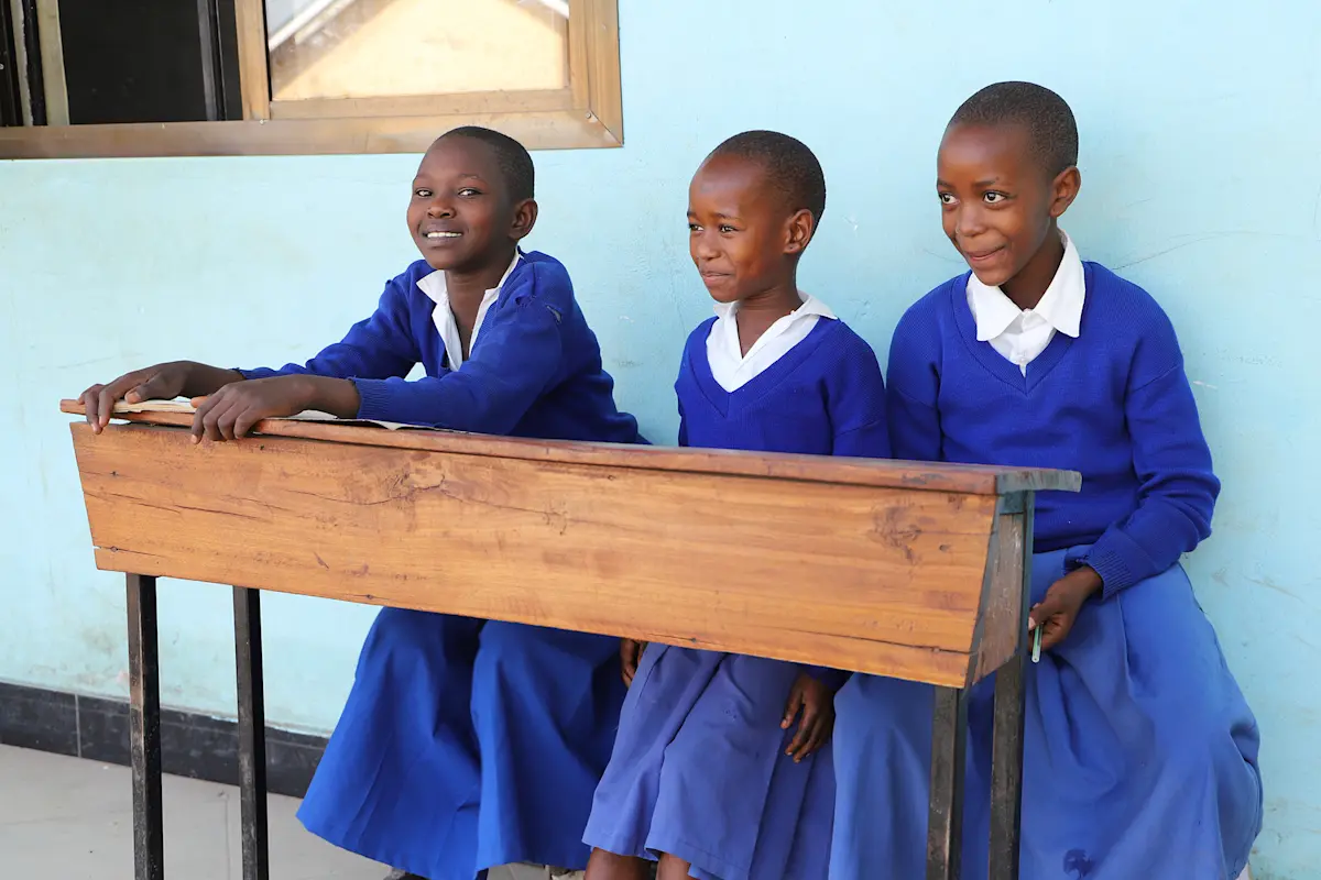 Three schoolgirls in blue uniforms sitting at a wooden desk