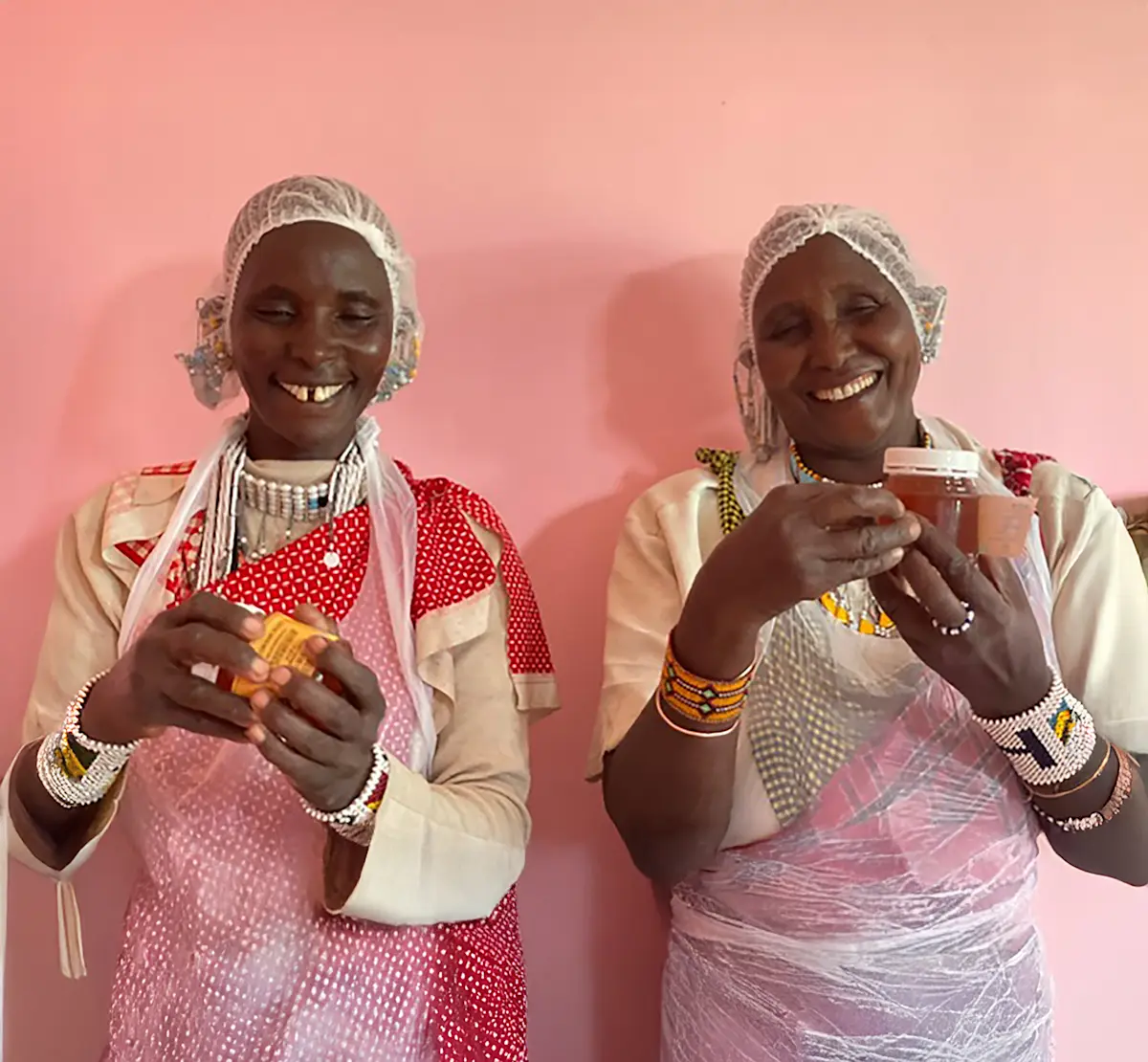 Two Maasai women in hairnets holding jars of honey