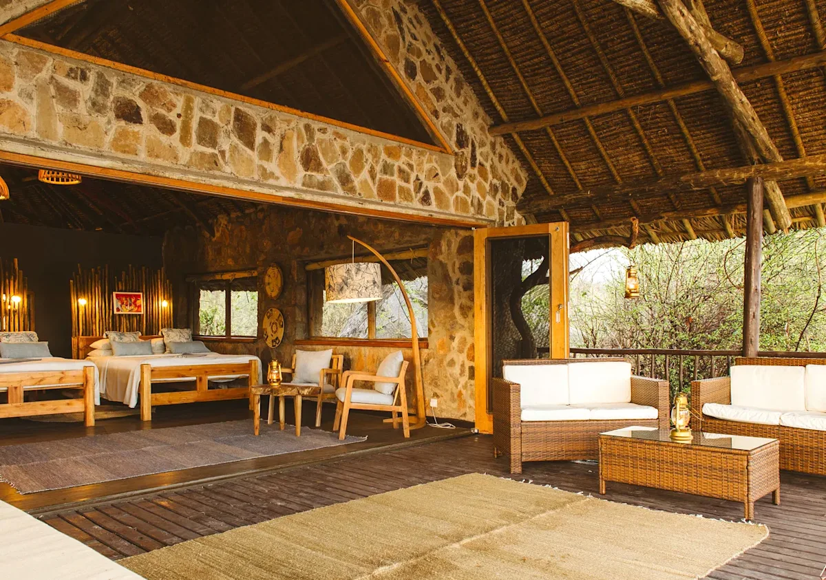 Open-sided stone and thatch room with beds and a sitting area at Ruaha River Lodge