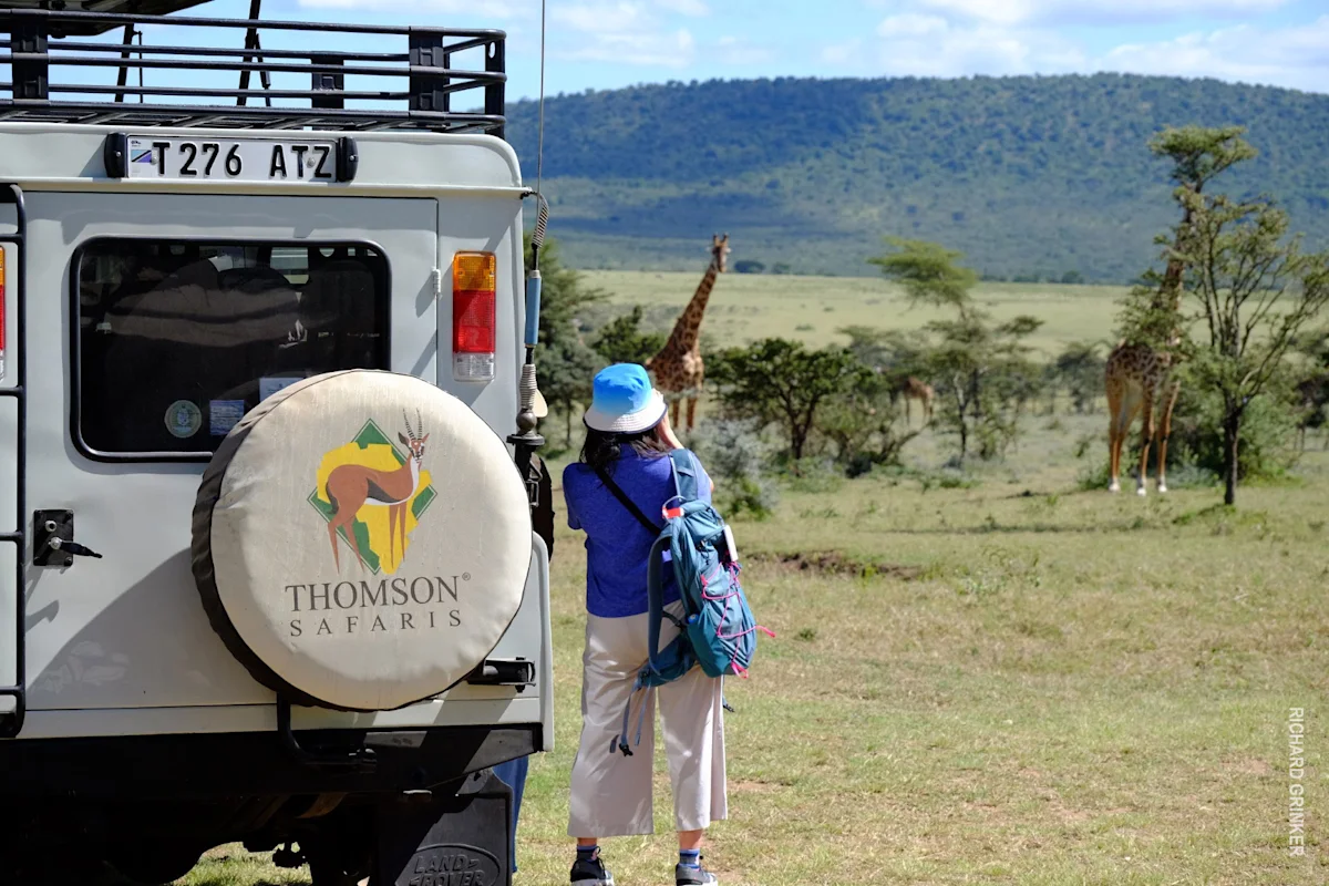 Traveler photographing giraffes beside a Thomson Safaris vehicle