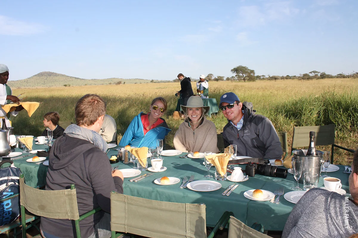 Travelers sharing a meal at a table set out on the grassland after a balloon ride