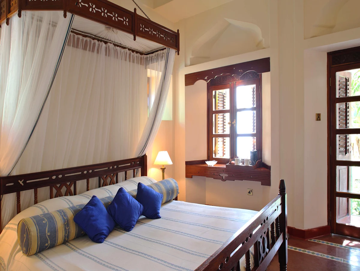 Carved wooden bed with blue pillows and a canopy at Zanzibar Serena Hotel