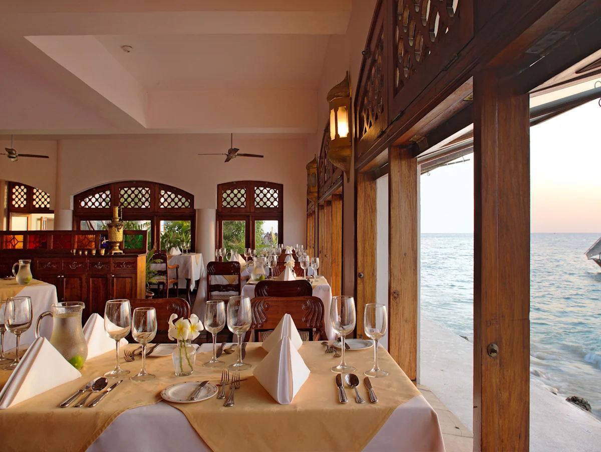 Restaurant with set tables and open windows onto the sea at Zanzibar Serena Hotel