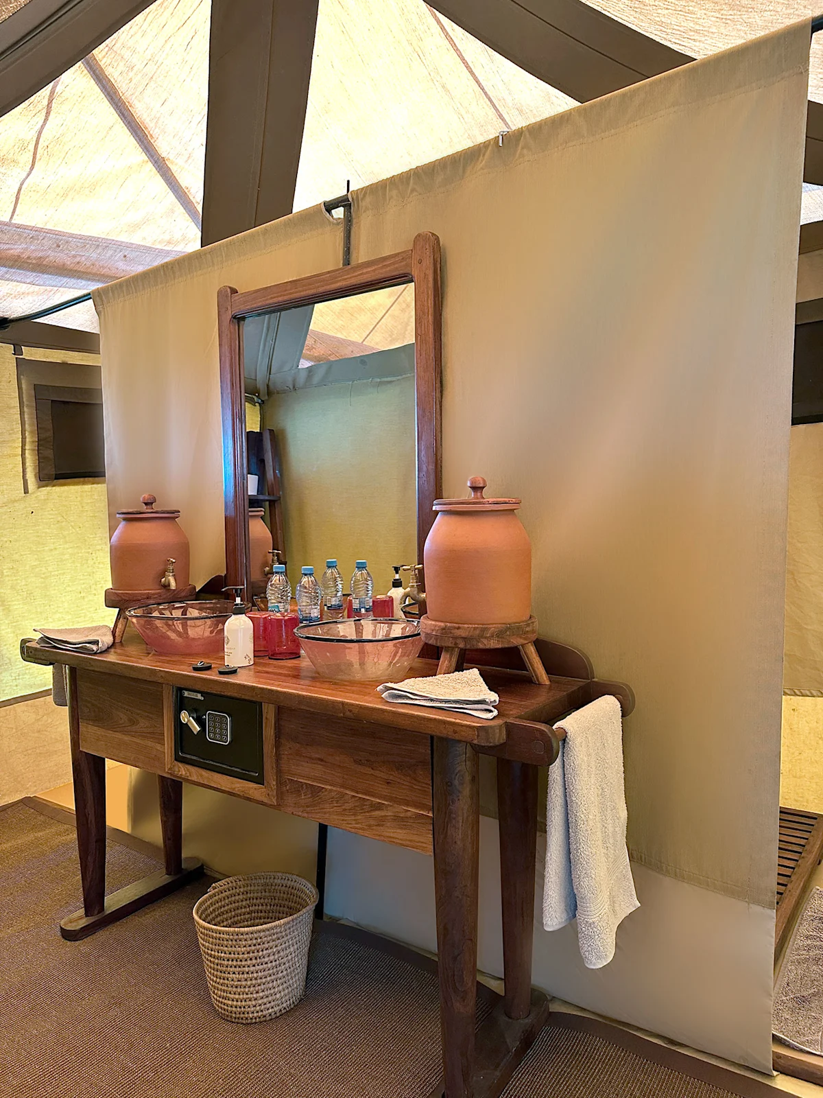 Wooden vanity with ceramic water jugs and a mirror inside a safari tent bathroom