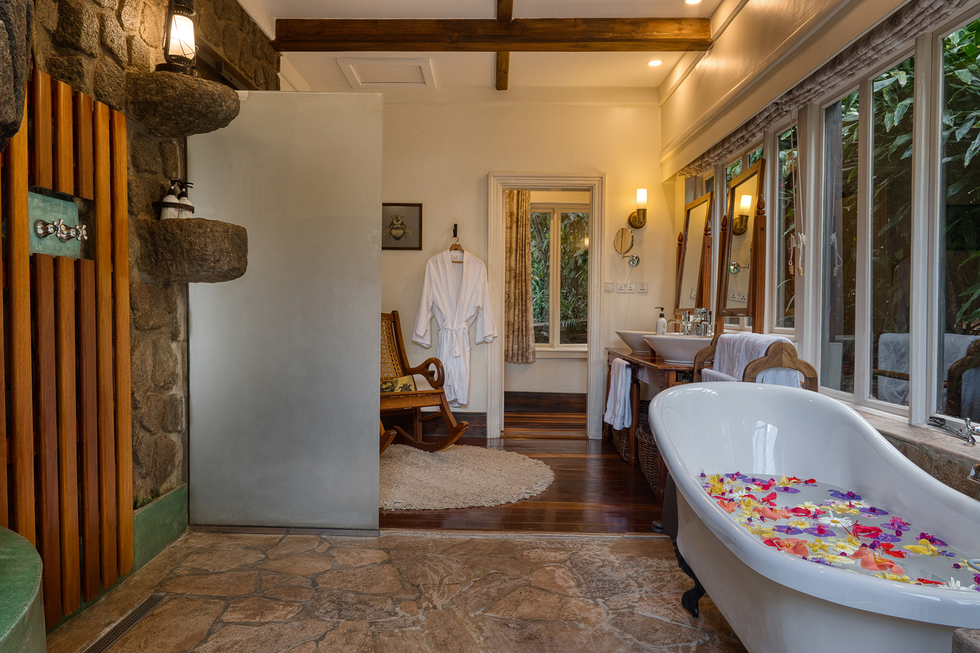 Gibb's Farm bathroom with a stone floor, glass shower and petal-filled clawfoot tub