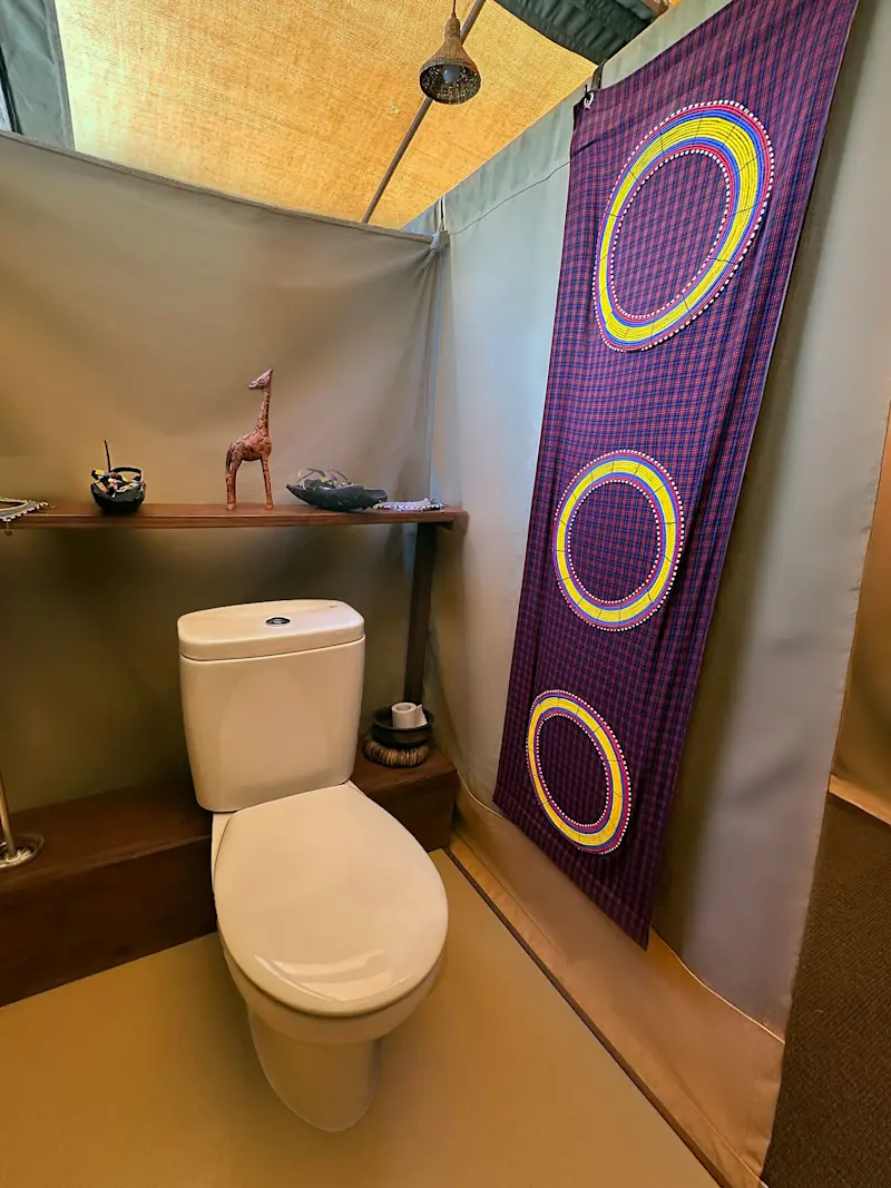 Flush toilet in a canvas tent bathroom with a Maasai-patterned wall hanging