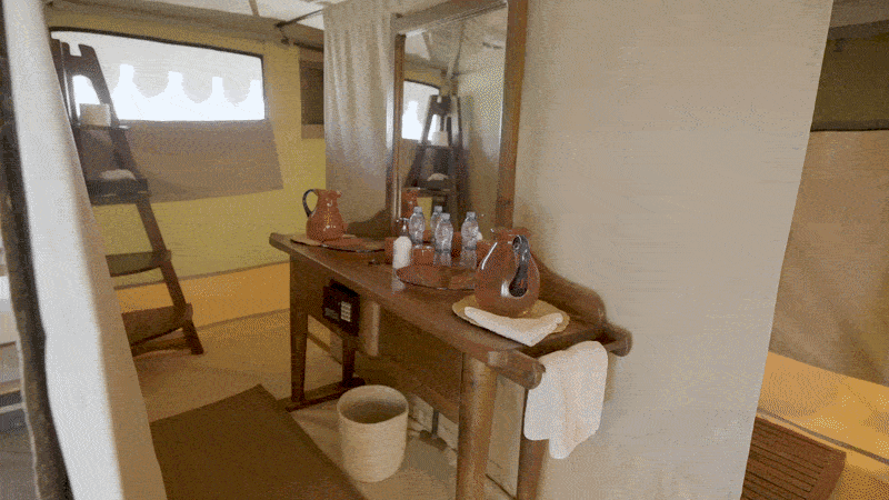 Tent bathroom with a wooden vanity and mirror leading back to the shower