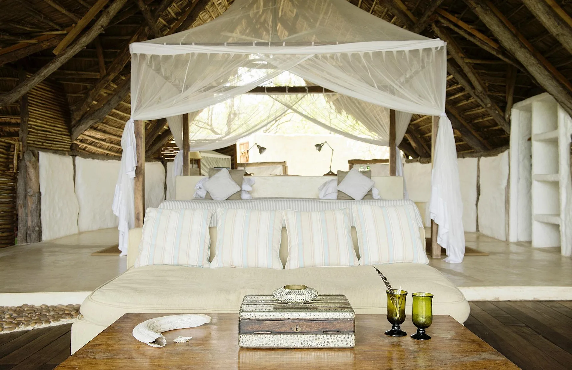 Canopy bed with white netting under a thatched roof at Sand Rivers