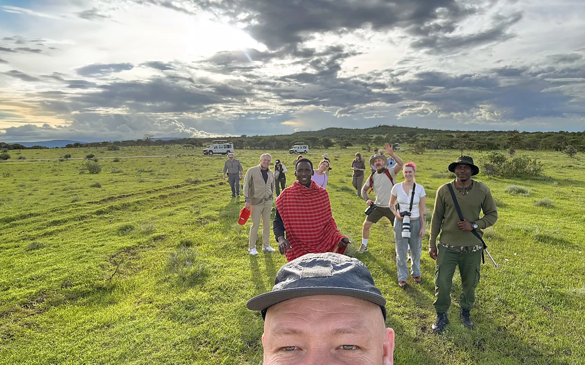 Selfie of a traveler with a walking safari group, a Maasai guide, and an armed ranger on green plains