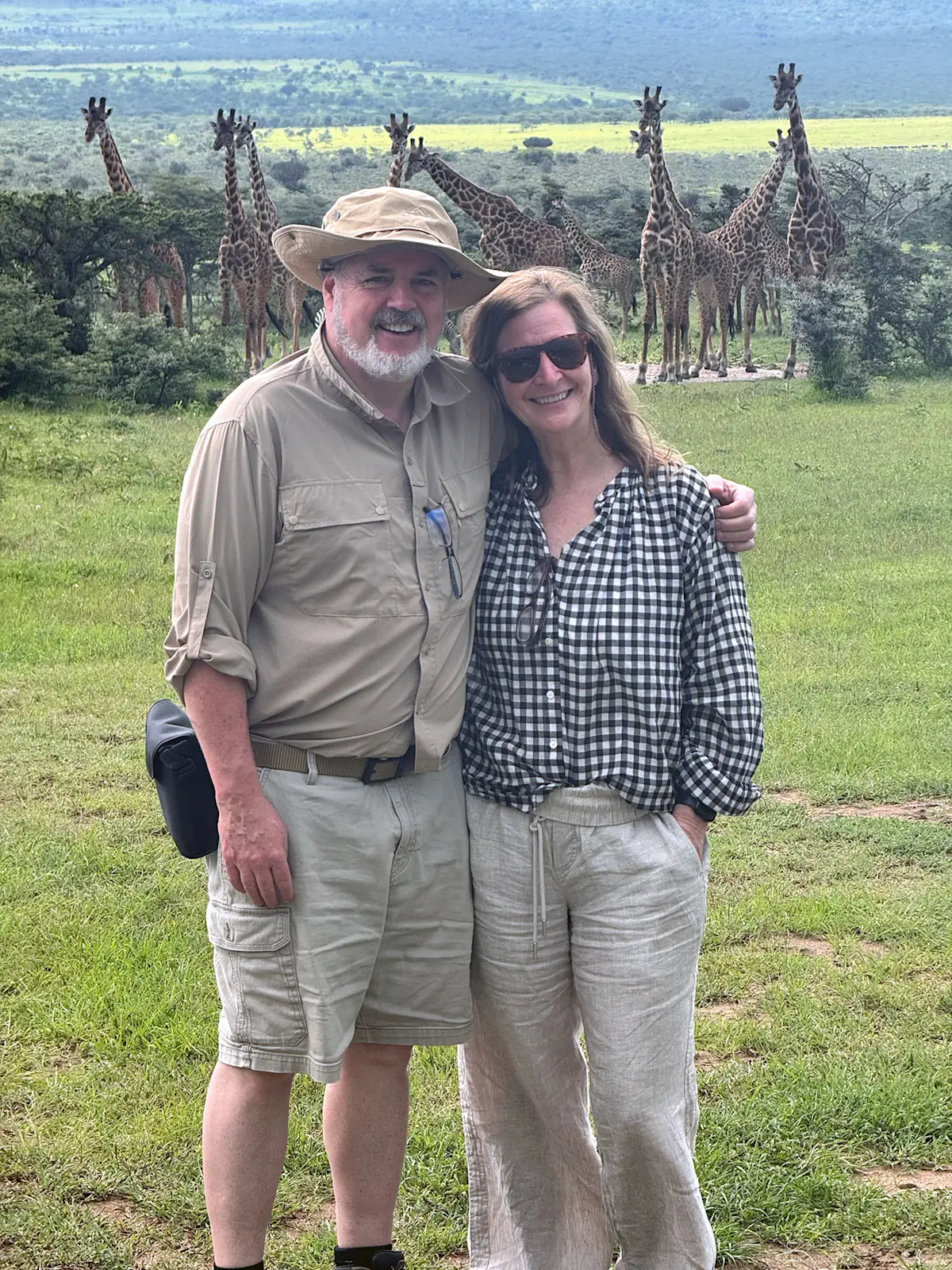 Couple posing on the savanna with a group of giraffes behind them