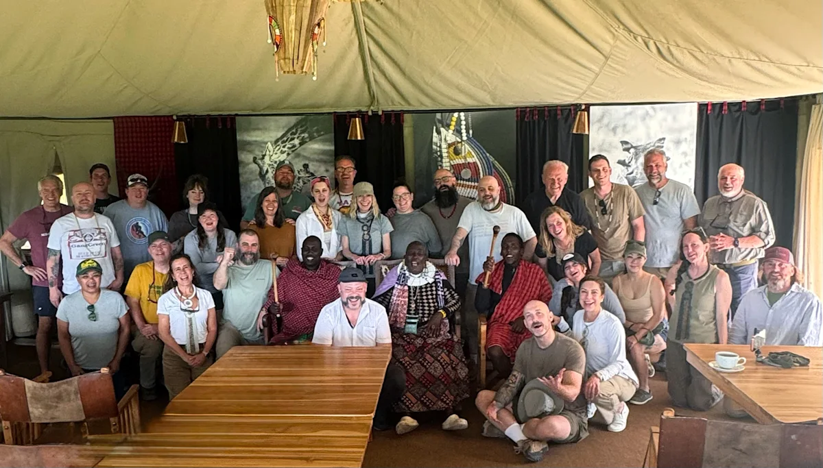 Large group of travelers and staff posing together inside a dining tent