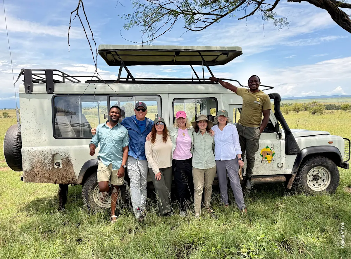 thomson safaris group poses in front of safari vehicle in serengeti