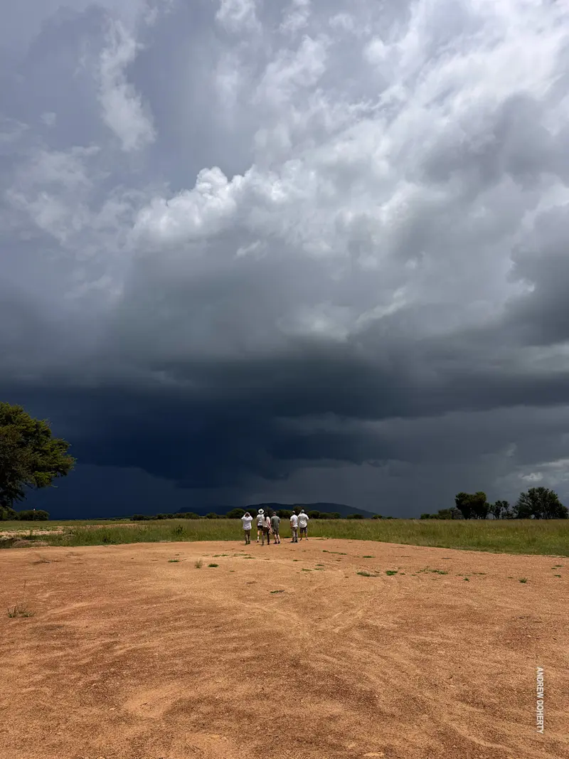 Small group of walkers on red earth beneath dark storm clouds