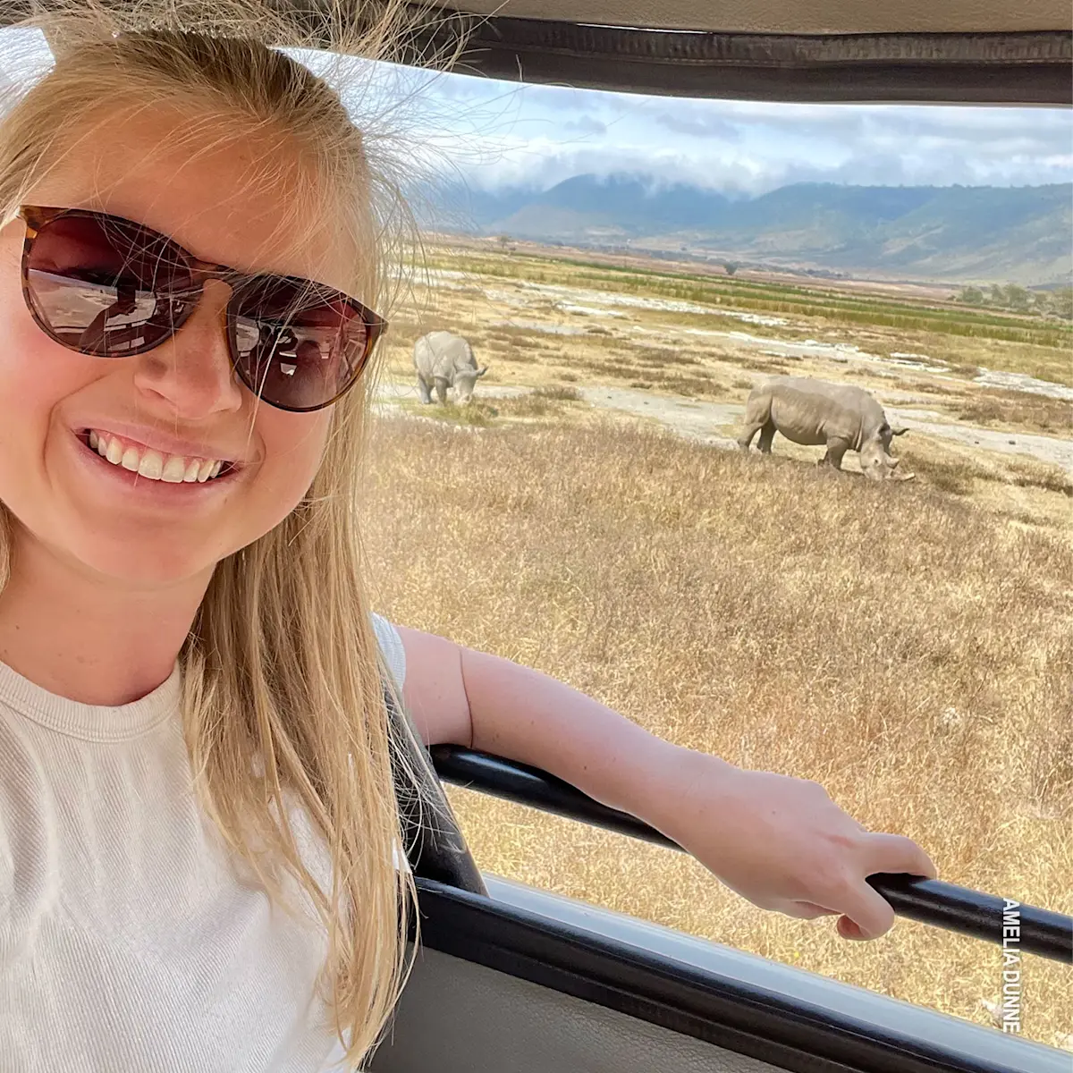 Woman smiling from a safari vehicle with white rhinos grazing behind in Ngorongoro Crater