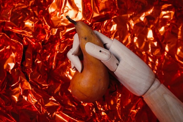 En træhånd, der holder en pære mod en rød, skinnende foliebaggrund.