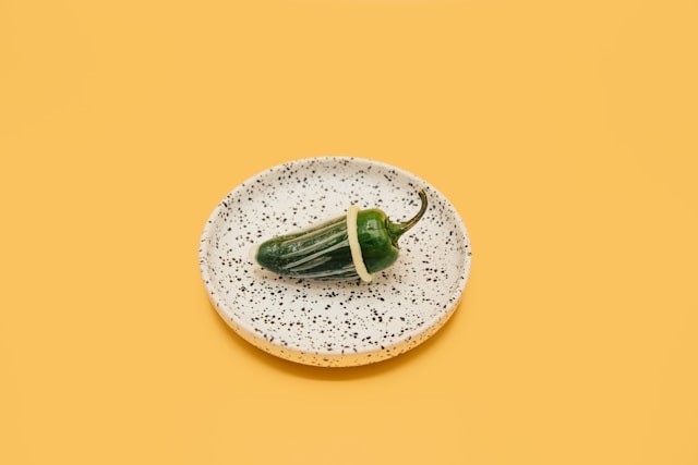 En grøn jalapeño-peber med kondom ligger på en spættet tallerken på gul baggrund.