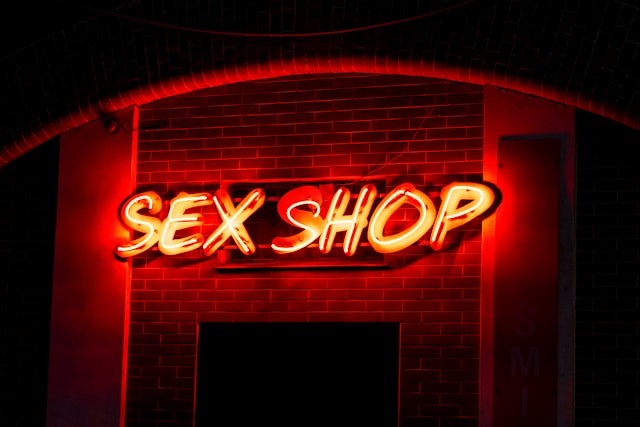 Et rødt neonskilt med teksten SEX SHOP oplyst på en murstensfacade om natten.