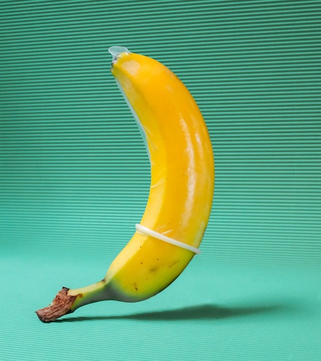 En banan med et kondom på, stående foran en grøn stribet baggrund.