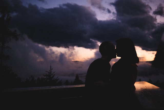a couple standing under a cloudy sunset sky kissing