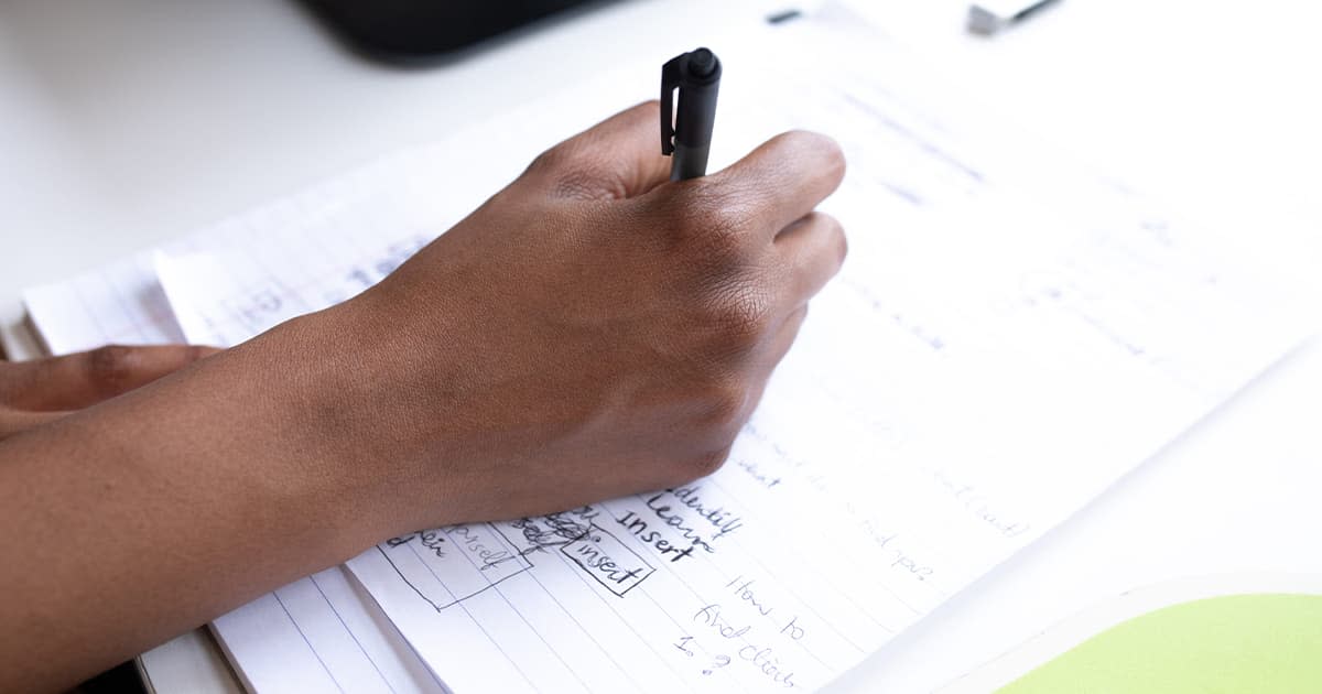 A hand holding a pen writing some plans down on a sheet of paper