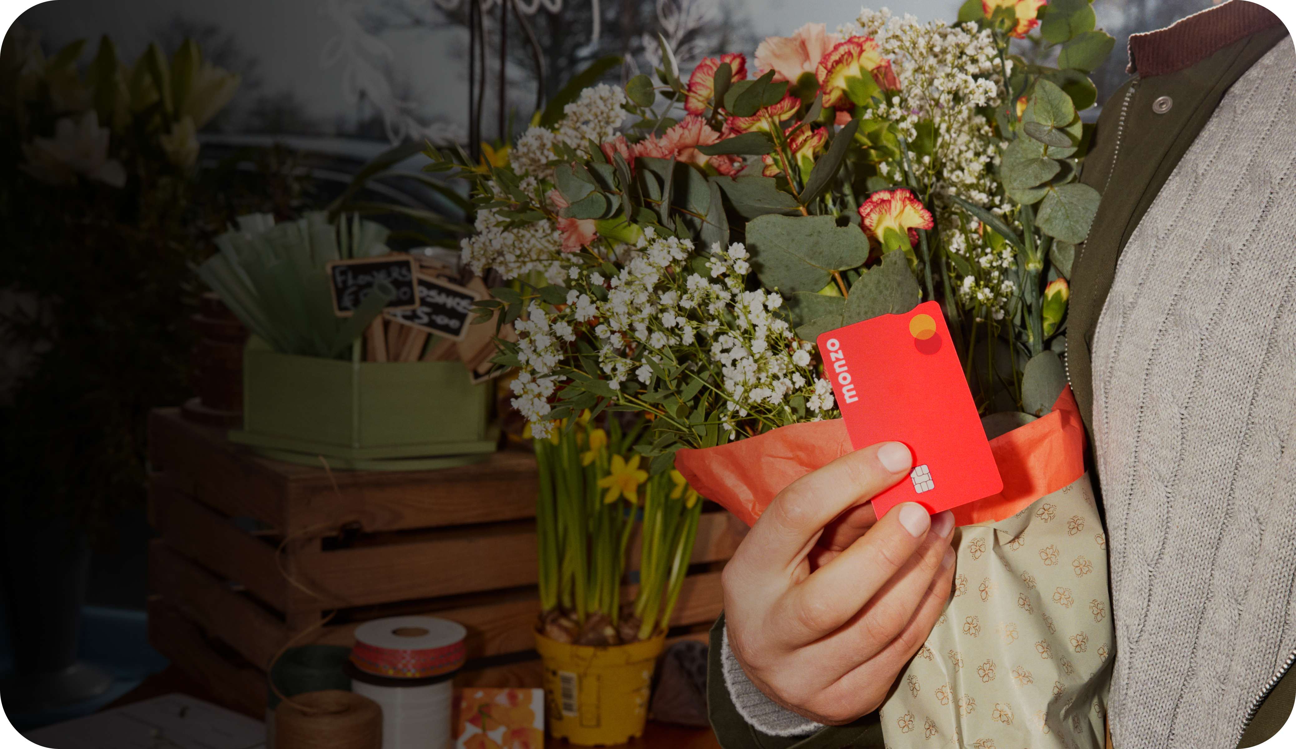 Someone holding their Hot Coral Monzo card against some bright blooms.