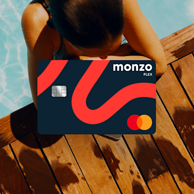 A woman in a pool, resting on the edge between the blue water and wood deck. A Monzo Flex card is laid over the top.