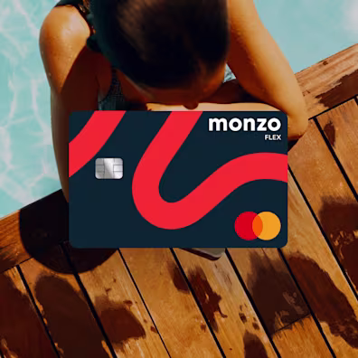 A woman in a pool, resting on the edge between the blue water and wood deck. A Monzo Flex card is laid over the top.