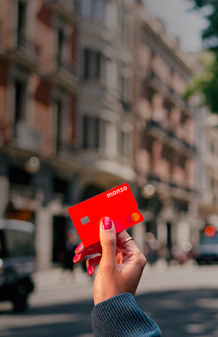 A person's hand holding a Monzo hot coral bank card with a visible chip