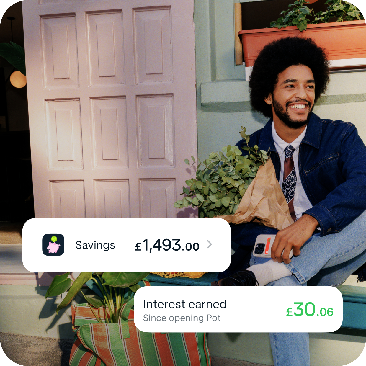 A man wearing double denim smiling sat on a porch in the sun. He's carrying a bunch of flowers. Overlaid is the Monzo Savings notification showing a savings total of £1,493.