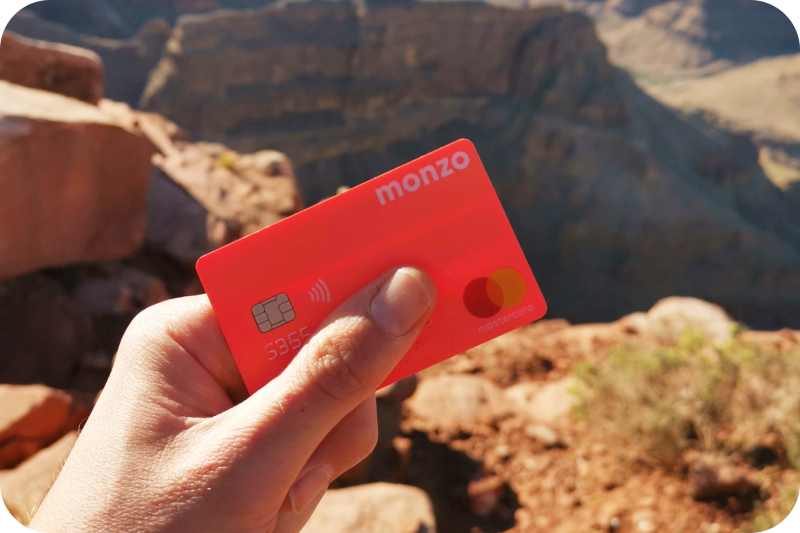 Person holding a Monzo card with rocky terrain in the background.