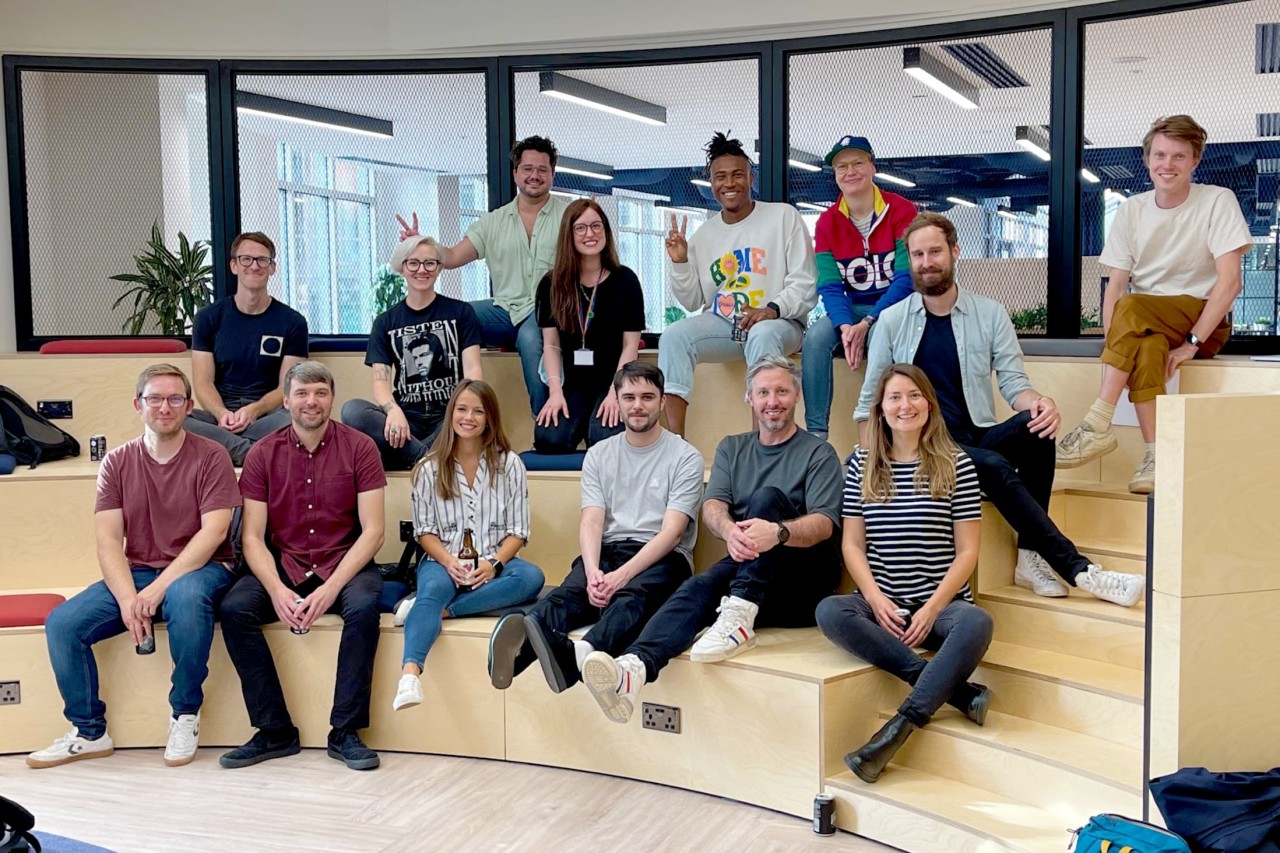The Monzo Design team - about 15 people - sitting on some wooden steps in the office