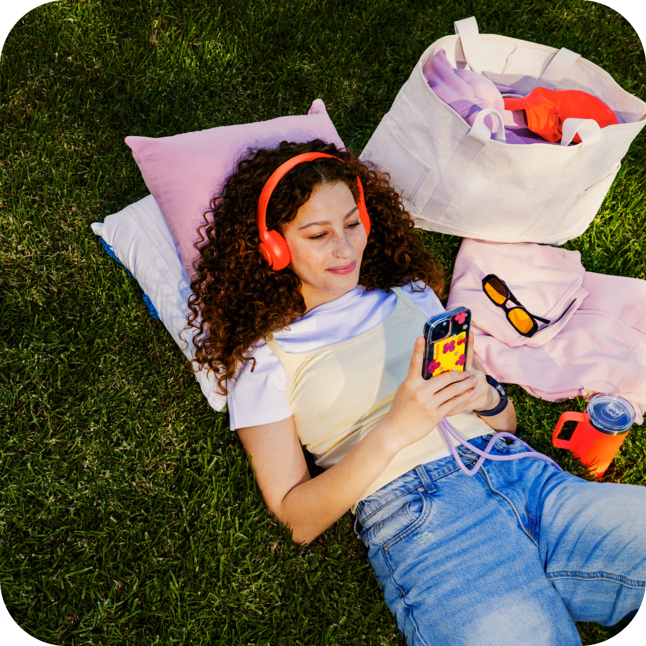 A woman lies in a blanket with headphones on, looking at her phone