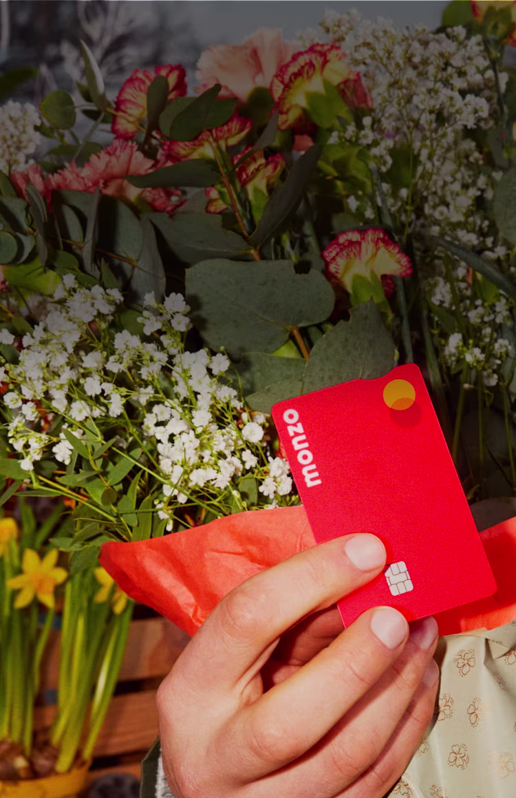 Someone holding their Hot Coral Monzo card against some bright blooms.