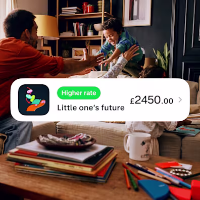 A family playing together in a living room, partially overlaid by a Monzo app notification showing a 'Little one's future' savings pot with a balance of £2450.00 and a 'Higher rate' badge.