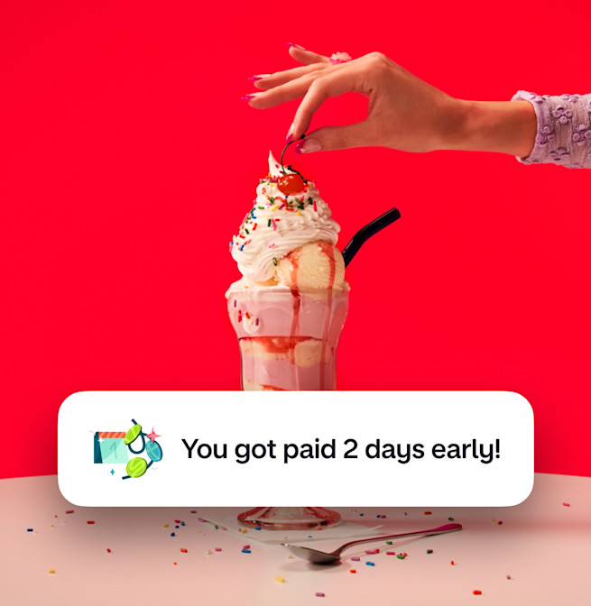 A woman's arm putting a cherry on top of an ice cream sundae against a red background. There is an image of a calendar with coins around it and text next to it saying You got paid two days early!