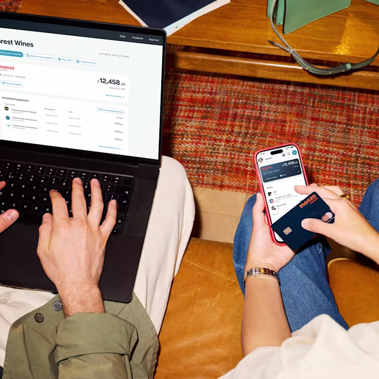 Two colleagues working together with a laptop, a phone showing the Monzo Business app and a Monzo Business bank card