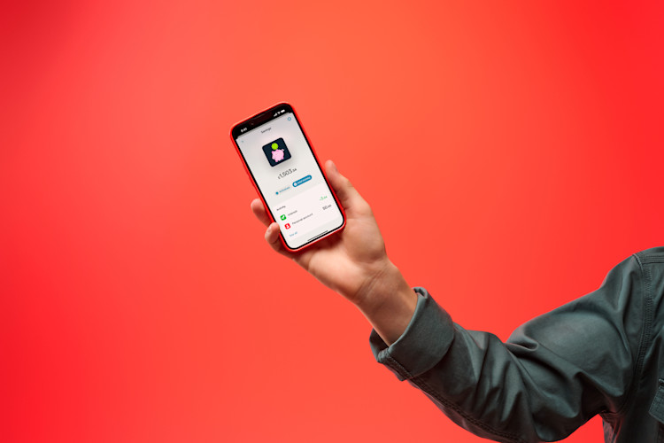 A person's arm holding a red smartphone showing the Monzo app's saving pots feature.