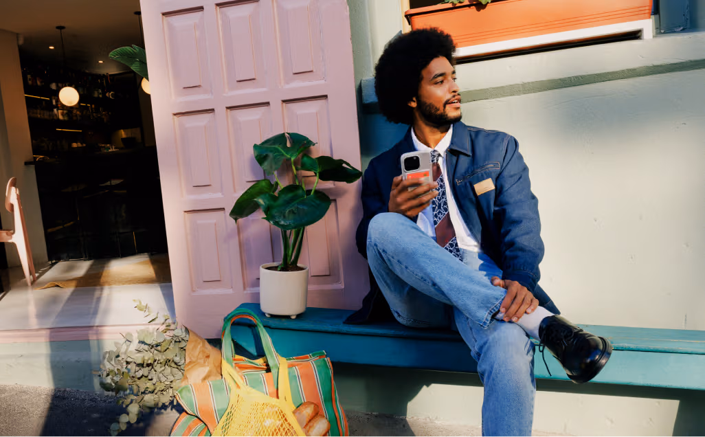 A man sitting on an outside bench looking at his smartphone.
