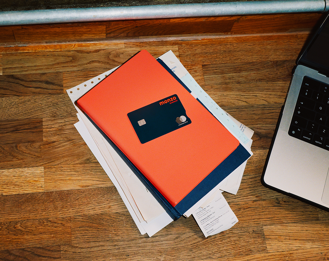 Monzo business debit card on a hot coral notebook next to a laptop