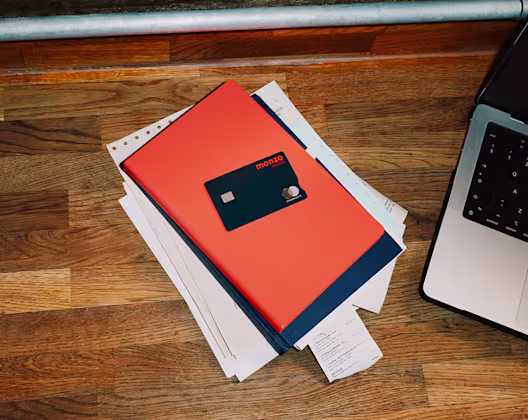 Monzo business debit card on a hot coral notebook next to a laptop