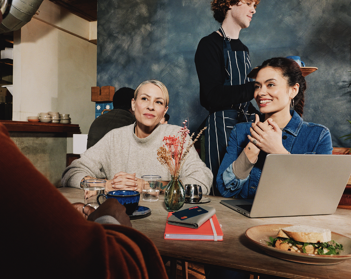 Two women behind a table with a laptop and a notebook on it