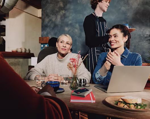Two women behind a table with a laptop and a notebook on it